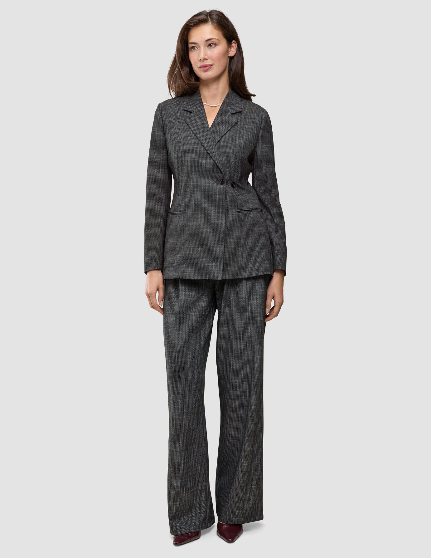 Eine Frau, die einen Women Nara Blazer Fitted Black Check in anthrazitgrauem Karomuster trägt, dazu eine passende Hose mit weitem Bein.